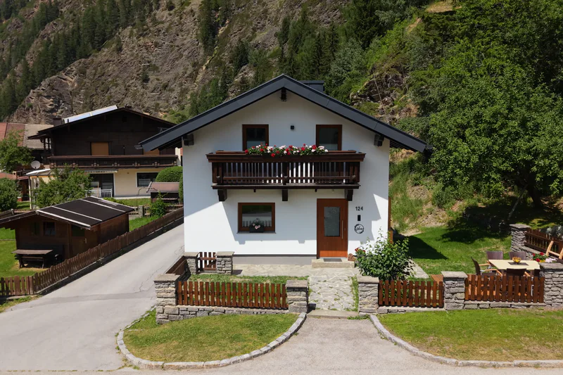 Irmas Ferienhäusl im Sommer von vorne: Balkon voller Geranien, davor Garten und Holzterrasse
